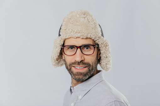 Stylish man in a cozy winter hat displaying a lighthearted smile on a plain background.