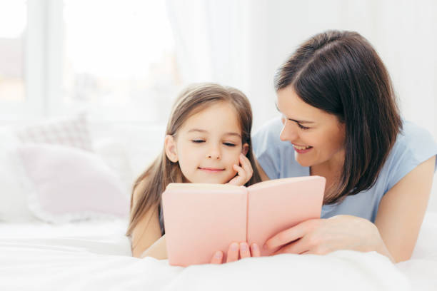 istock A cozy moment shared between mother and daughter as they read a book together on a bed. 2151260418