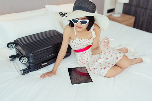 The young Asian woman, clad in a fashionable hat and dress, arrives at the deluxe hotel with her suitcase, laptop, filled with anticipation for the festival and eager for a summer retreat.