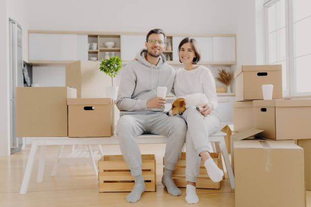 istock Smiling couple taking a break on boxes, dog nestled between them. 2151263168