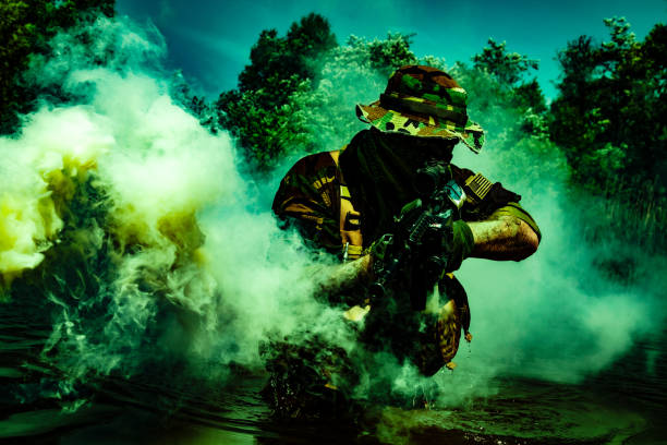 A bearded soldier performs a surveillance task in the water, walking through a swamp, surrounded by mist fog, rifle at the ready for imminent threats, colorized toned shot
