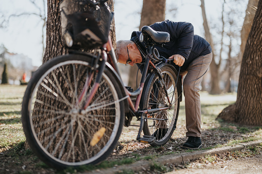 Senior man checking bicycle tire in park - everyday active lifestyle concept.