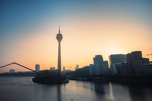 The beautiful sunrise casts a warm glow over the Rhine Tower and the modern skyline of Dusseldorf, Germany.