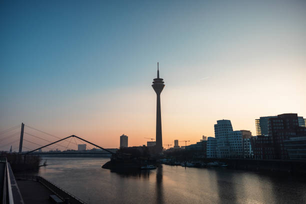 A scenic sunset over the Dusseldorf skyline, highlighting the iconic Rhine Tower and the calm waters of the Rhine River.