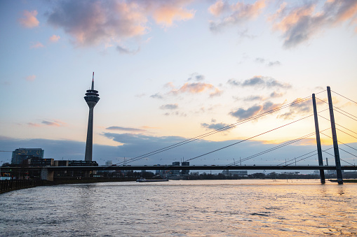 The Rhine Tower and a bridge at sunset with pastel-hued skies reflecting in the Rhine River, showcasing the beauty of Dusseldorf.