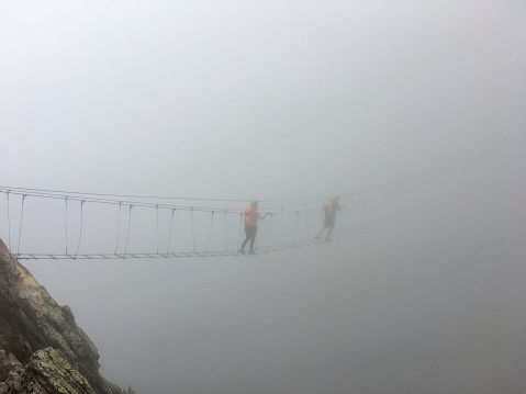 Climbers cross suspension bridge in fog on a Via Ferrata route
