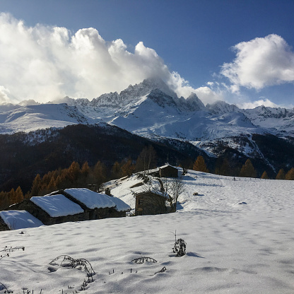 Fresh powder snow covers mountain meadow and village below mountain peak