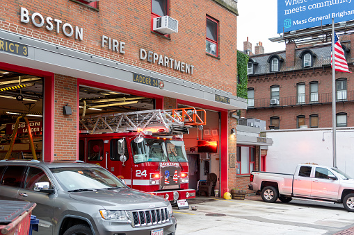 Fire Station in Boston, Massachusetts, USA.  There are cars parked and a fire engine driving out of the garage.