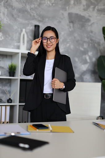 A young Asian businesswoman excelling in her career, working professionally in her office, with a confident and positive demeanor.