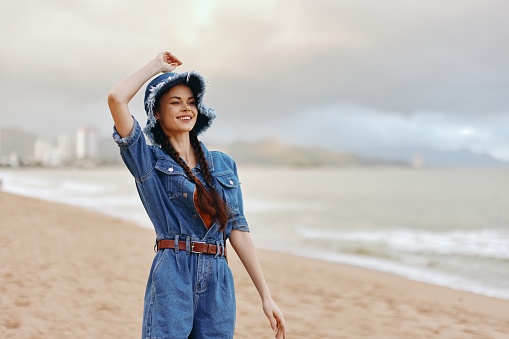 Free-spirited Young Woman Enjoying a Relaxing Summer Vacation, Standing on a White Sandy Beach with Ocean Waves in the Background