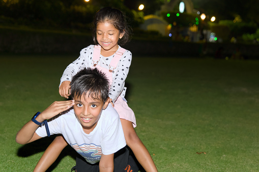 A joyful Indian brother and sister create lasting memories under the glow of park lights at night.