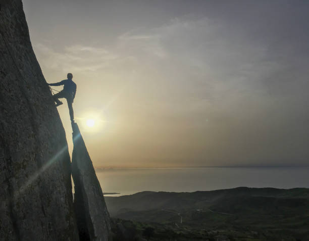 istock Man climbs rock spire above sea 2151294951