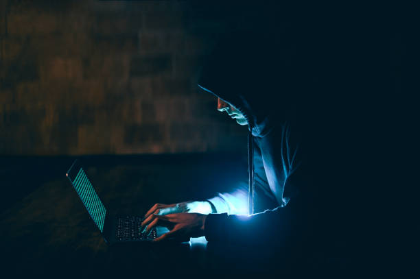 istock hooded hacker typing on laptop in a dark room, Cybersecurity 2151295156