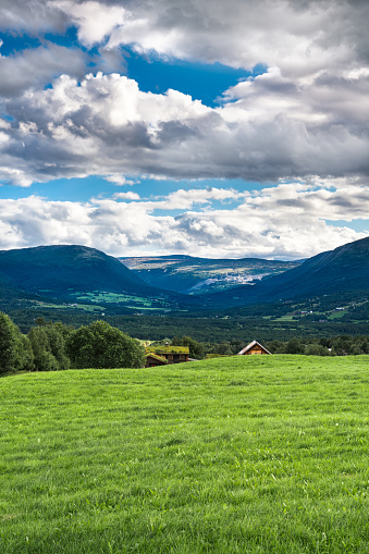 Lush grassland of Oppdal valley, in Trøndelag Norway with a farm tucked behind a rolling hill, under a sky filled with striking clouds.