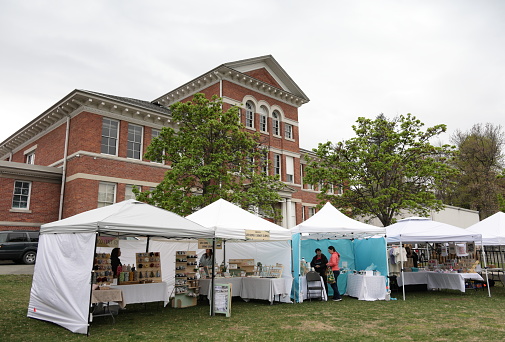 Kamloops, Canada - April 27, 2024: Vendors and customers attend the Farmers Market held at the 200-block of St. Paul Street downtown. Historic Stuart Wood School stands in the background. Spring morning with overcast skies.