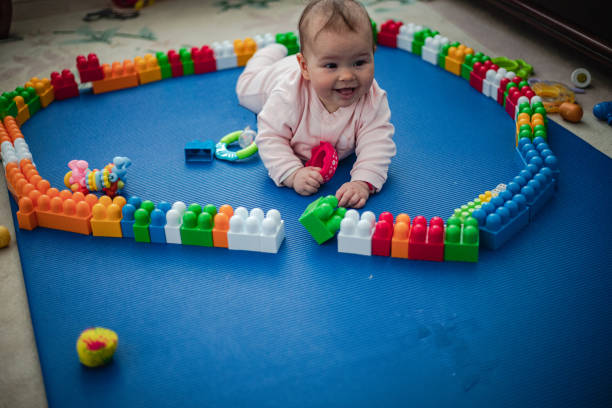 A latin baby girl sitting and playing with toy blocks in a horizontal full length studio shot with white background.