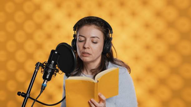 istock Narrator wearing headset reading aloud from book into mic, studio background 2151325445