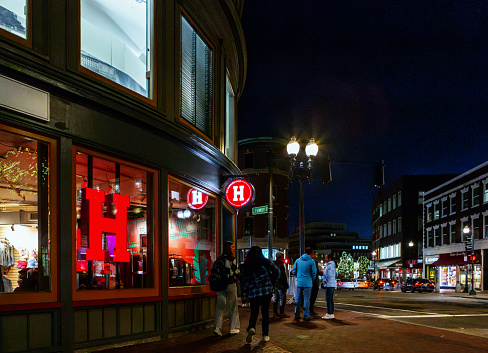 Cambridge, Massachusetts, USA - May 1, 2024: Night scene at the center of Harvard Square, the intersection of JFK Street, Brattle Street and Massachusetts Avenue. On the left is The Harvard Shop retail store, seller of Harvard University souvenirs and apparel.