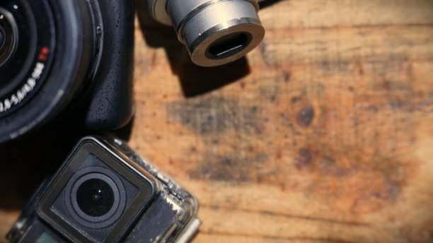 POV: cameras on a wooden table. A professional zoom camera, an old action camera, and a small digital camera. Filmmaking tools. Cinematography table. Photography cameras ready to use. An overhead angle.