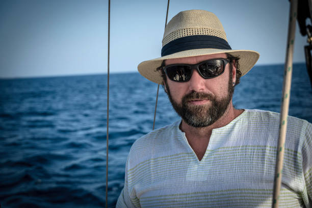 A man wearing a straw hat is driving a sailboat and enjoying it.