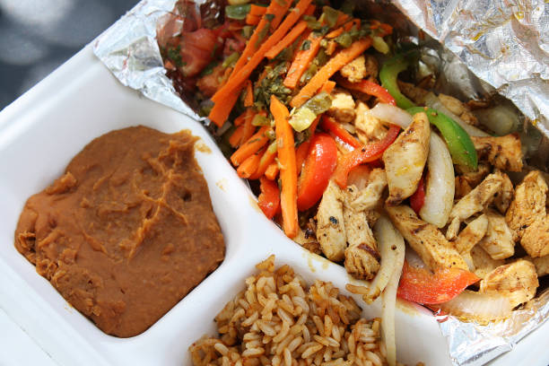 An image take from above of a fajita plate in a to-go container. On secton has chicken and vegatables, one has refried beans and one has mexican rice.