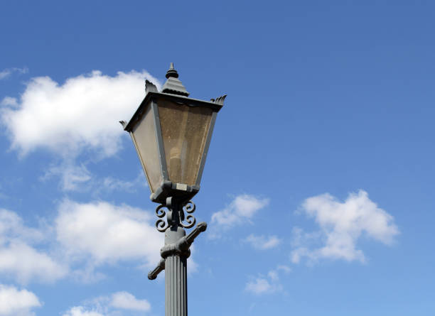 Old-fashioned street lamp and pole set against a blue sky with white clouds