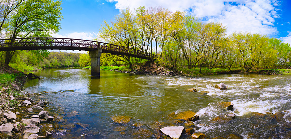 Tranquil beautiful spring forest landscape with the rustic footbridge and arching maple trees over the Big Sioux River at Parsly Park in Sioux Falls, South Dakota, USA