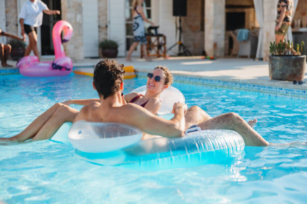 istock Hispanic Couple Lying On Inflatable Donuts And Relaxing In The Pool During  A Pool Party 2151338511