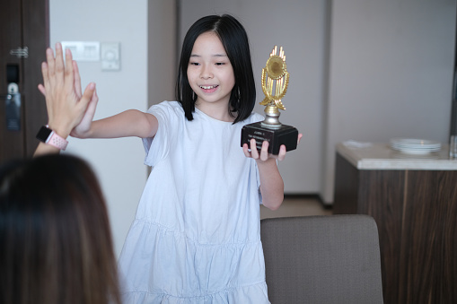 Close-up shot Asian little girl high five with her mother while holding her gold trophy
