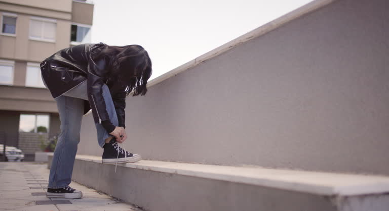 Young woman in a leather jacket tying her shoes on an urban balcony