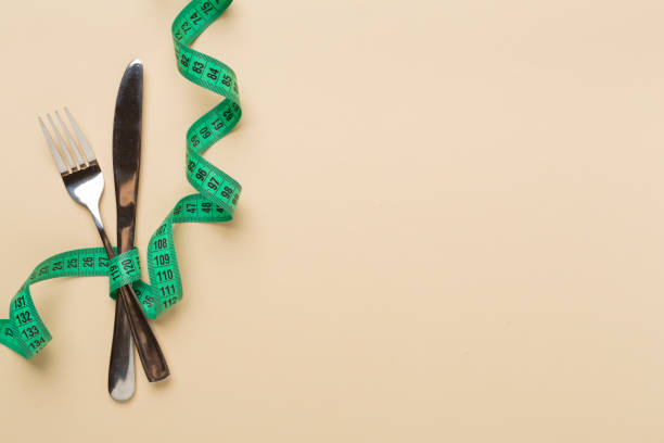 istock Knife and fork wrapped in tape measure on color background, top view 2151345847