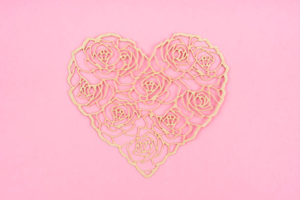A heart shape cut out of pink paper that exposes a bed of red roses.