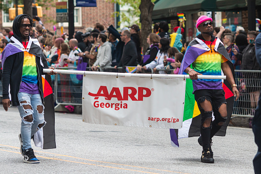 Atlanta, GA / USA - October 15, 2023:  Two African-American men wearing pride colors carry an AARP banner as they walk down Peachtree Street in the annual pride parade on October 15, 2023 in Atlanta, GA.