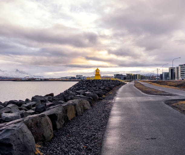 A lighthouse facing the snow-capped mountains by the sea.