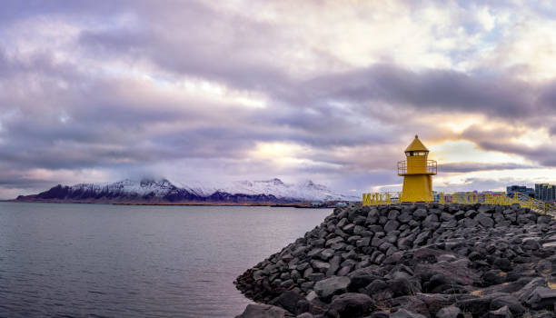 A lighthouse facing the snow-capped mountains by the sea.