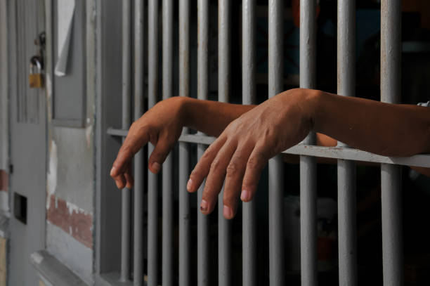 istock hands of a prisoner behind prison bars 2151366320