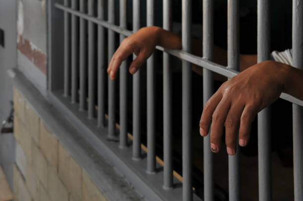 istock hands of a prisoner behind prison bars 2151366335