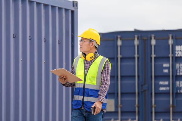 istock Engineer man in industry containers cargo, Foreman dock worker in a hardhat and safety vest control loading containers box from cargo 2151368456