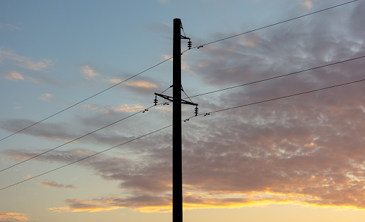 Electric pole with wires against the backdrop of the sunset.