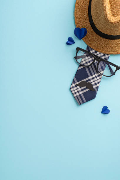 istock Mark Dad's special day with heartwarming vertical scene featuring top view of straw hat, sophisticated necktie, glasses, mustache, hearts on soft blue backdrop, perfect for your messages or promotions 2151372297