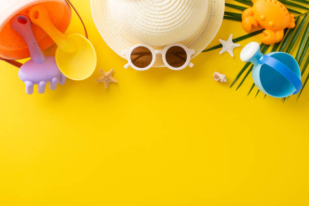 istock Bright and colorful summer beach accessories including a straw hat, sunglasses, and various children's beach toys laid out on a vivid yellow background 2151372317