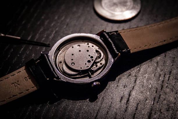 This detailed close-up photograph captures the inner workings of a mechanical wristwatch. The back cover of the watch is removed, revealing the intricate gears, springs, and components of the timepiece. The focus on the watch mechanism highlights the precision and craftsmanship involved in horology. The image is set against a dark background, with a soft, warm light that accentuates the metallic textures and fine details. This photograph beautifully showcases the complexity and artistry of traditional watchmaking.