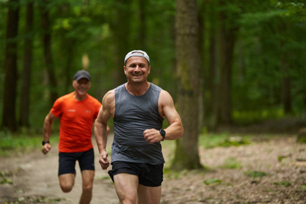 Two male friends running together on a trail through the forest