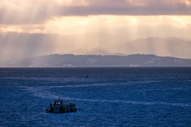 Ajaccio, France - March 19, 2024. Sunrise view over the Mediterranean sea in Ajaccio bay. The rays of sunlight piercing the clouds light up the mountains.