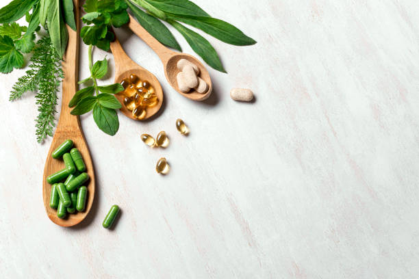 Natural organic supplements and vitamins Natural vitamins, plant based supplements and green leaves on white wooden background, top view, copy space. Various organic capsules and pills, creative flat lay. nutritional supplement stock pictures, royalty-free photos & images