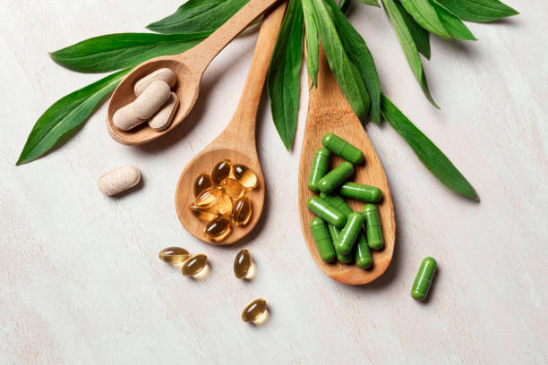 Suplementos orgânicos naturais e vitaminas. Cápsulas de suplementos e vitaminas em colheres de pau com folhas verdes de plantas em fundo branco, vista superior, flat lay. Suplementos orgânicos naturais, conceito de estilo de vida saudável. Fotos de suplementos, fotos e imagens livres de direitos autorais.