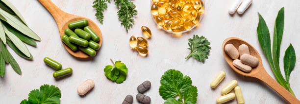 Natural vitamins, plant based supplements Natural vitamins, plant based supplements and green leaves flat lay on white wooden background. Various organic capsules and pills, banner. healthcare fitness and herbal medicine banner set stock pictures, royalty-free photos & images
