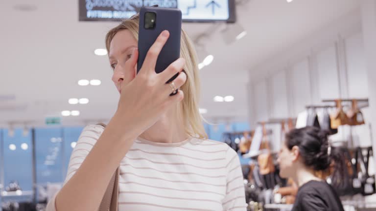 Beautiful female customer shopping in clothing store using smartphone