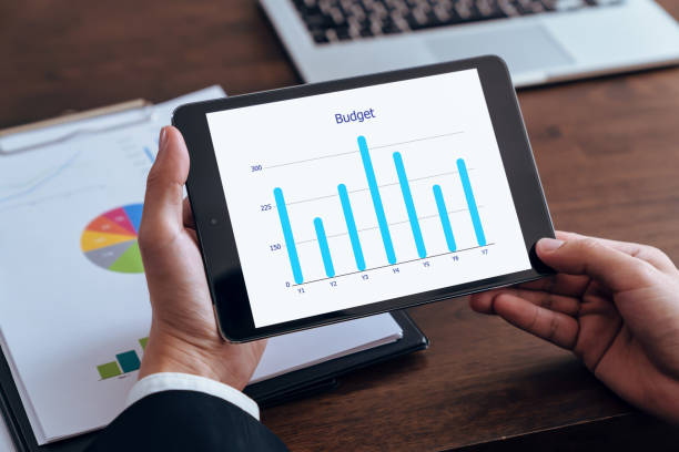 istock Businessman holding tablet and showing budget graph screen with financial documents on the table. 2151408845