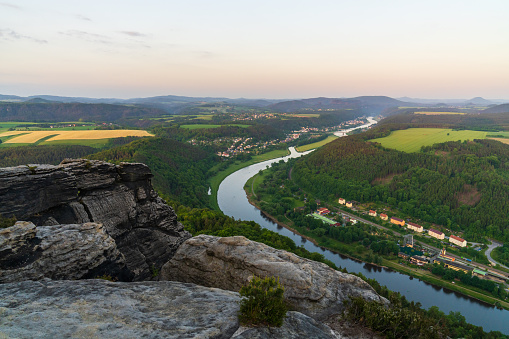 Early morning in the Saxon Switzerland National Park. View from the high cliff of the crooked Elbe River, green fields and meadows in the valley. Life awakens in beautiful German houses